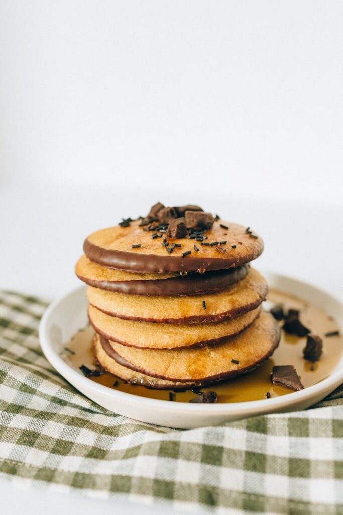 Appetizing stack of chocolate-coated pancakes drizzled with syrup on a white plate.