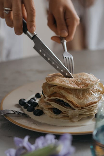 Close-up of a pancake stack with blueberries being sliced, perfect for breakfast or dessert.